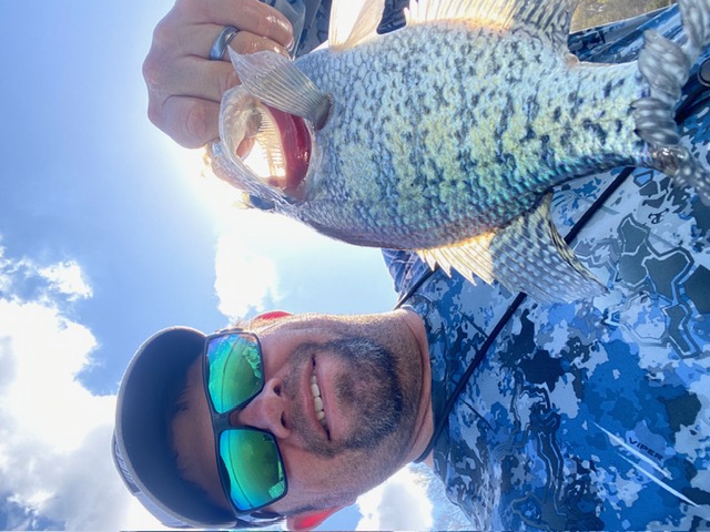 Mike holding a crappie beneath a bright lake sky